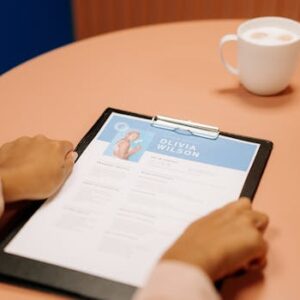 Close-up of hands holding resume during interview with coffee on table, highlighting workplace setting.