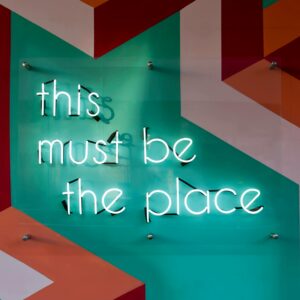 Colorful geometric wall featuring a glowing neon sign with an inspirational quote.