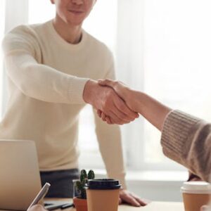 Close-up of professionals shaking hands over coffee in a modern office.