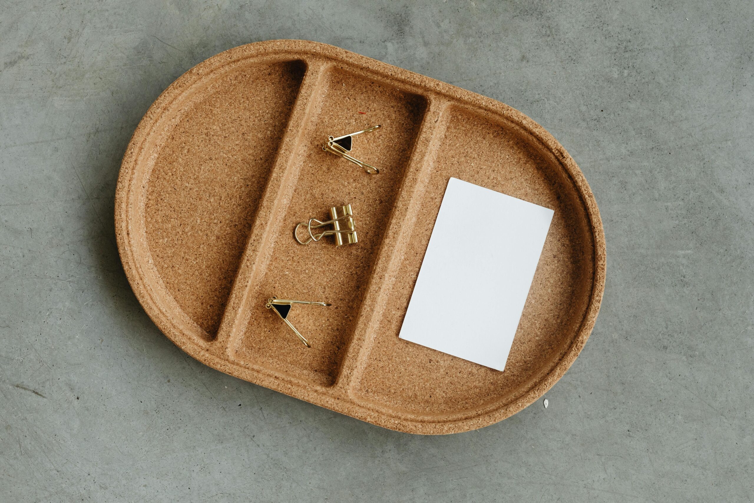 Simple cork tray with business card and binder clips on concrete.